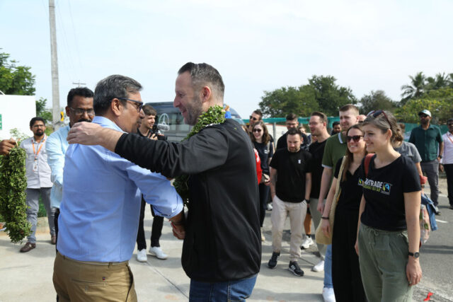 Auf dem Bild ist eine Gruppe Menschen zu sehen. Im Fokus stehen zwei Männer, die einander freundschaftlich begrüßen.