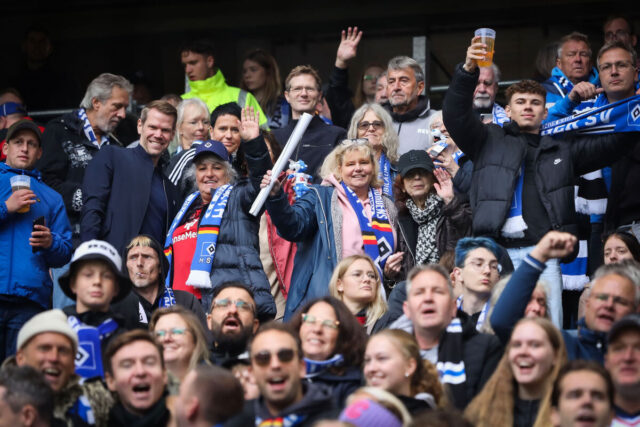 Das Bild zeigt eine Gruppe von Fans auf einer Tribüne im Volksparkstadion. Im Fokus stehen Frauen und Männer in Fankleidung und mit Bier in der Hand, die in die Kamera winken. Mit auf dem Foto ist HSV-Vorstand Eric Huwer zwischen den Fans zu sehen.