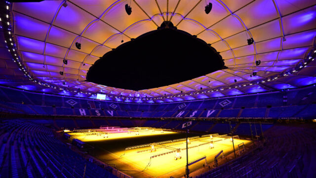 Das Bild zeigt eine Innenraumaufnahme des Volksparkstadions bei Dunkelheit. Auf dem Rasen stehen Lampen, welche die gesamte Breite des Platzes einnehmen. Sie beleuchten den Rasen.