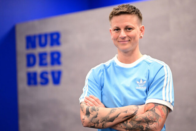 Das Bild zeigt Jobina Lahr. Sie ist eine Spielerin bei den HSV-Frauen. Sie steht vor einer grauen Wand, auf der links im Hintergrund in Blau „Nur der HSV“ steht. Lahr selbst trägt ein hellblaues Adidas-T-Shirt. Sie trägt schwarze Ohrstecker, hat kurze braune Haare und großflächige Tattoos auf den Unterarmen. Sie lächelt in die Kamera.